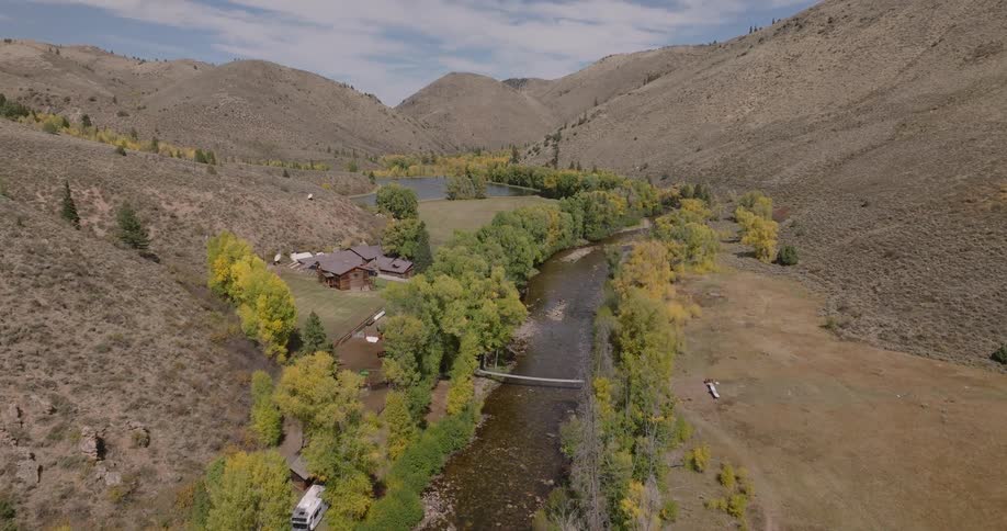 A ranch sits at the edge of a treelined river between the mountains