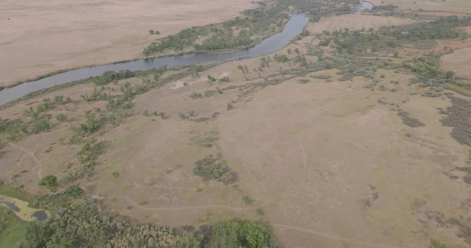 An aerial view shows a winding river flowing through a dry expansive landscape with scattered shrubs and trees