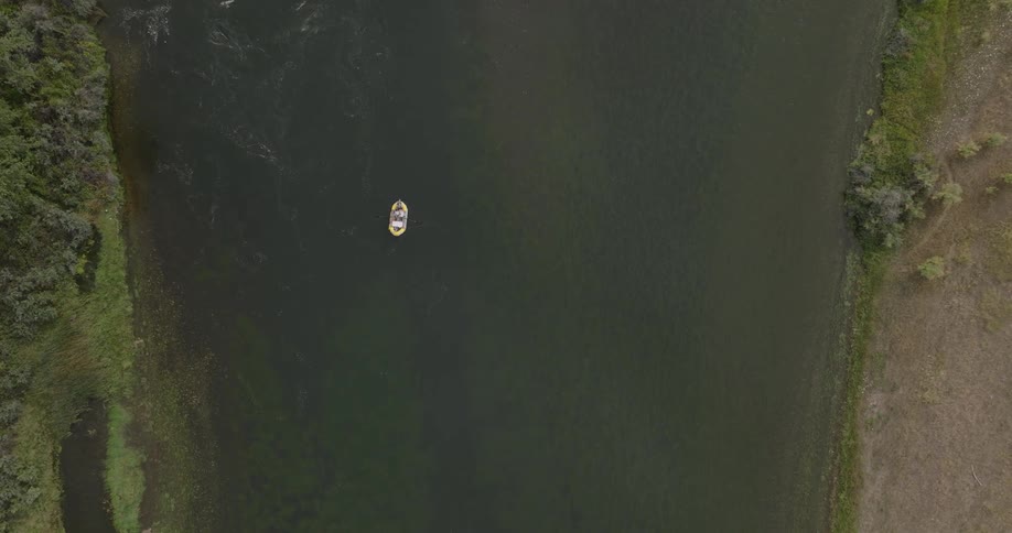 A lone boat floats on a calm river surrounded by greenery captured from directly above