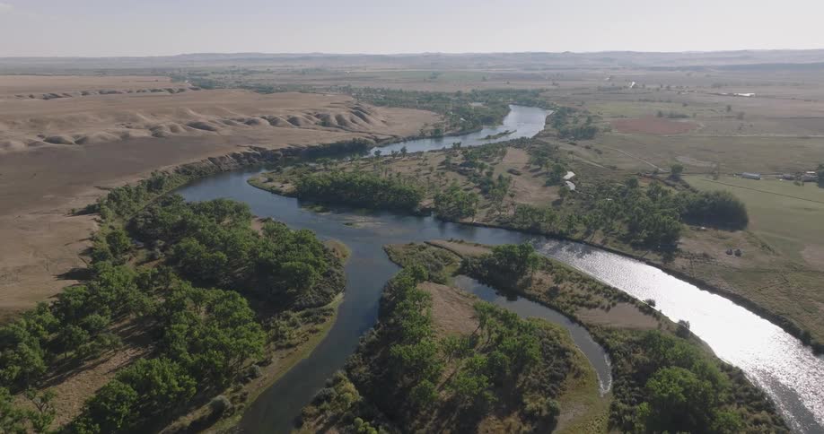 Aerial view of a winding river cutting through grassy plains and clusters of trees