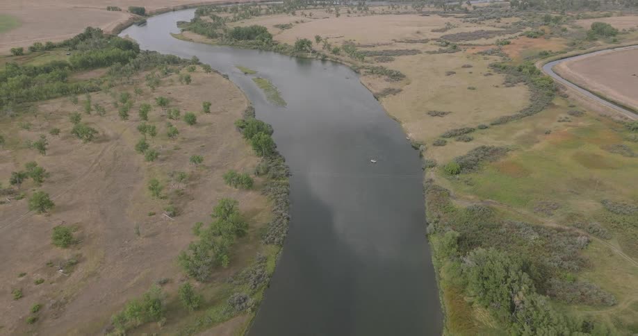 A winding river cuts through dry grasslands and scattered green trees