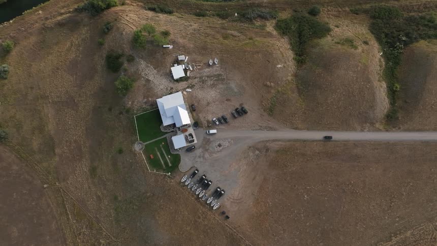 An aerial view of a rural property with buildings vehicles and boats on a dry grassy landscape