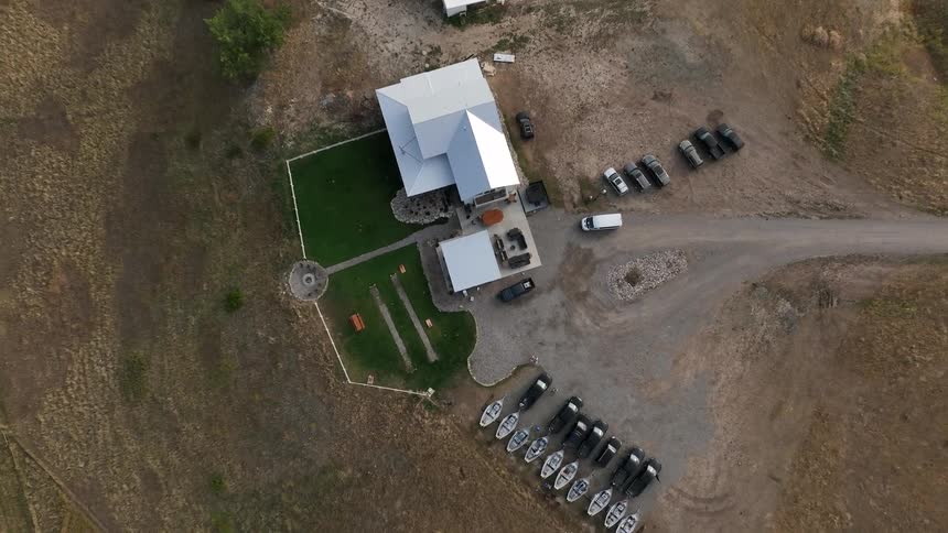 Aerial view of a house with parked vehicles and boats in a dry open rural area