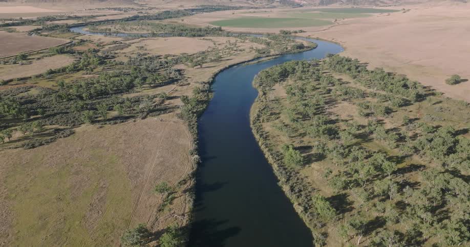 A slowmoving aerial view pulls back and tilts up to reveal a wide river winding through a vast valley of fields and farmland on a sunny day