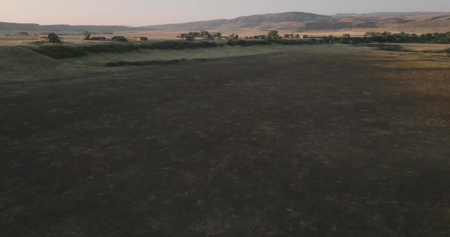 A wide open field stretches toward a rural village with distant hills under soft evening light