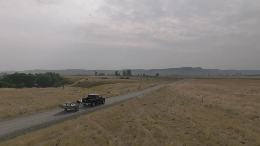 Pickup truck carrying a boat while traveling along a road with mountains on the horizon