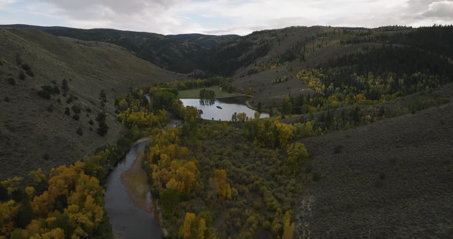 A river flows through a valley with autumn trees and a pond