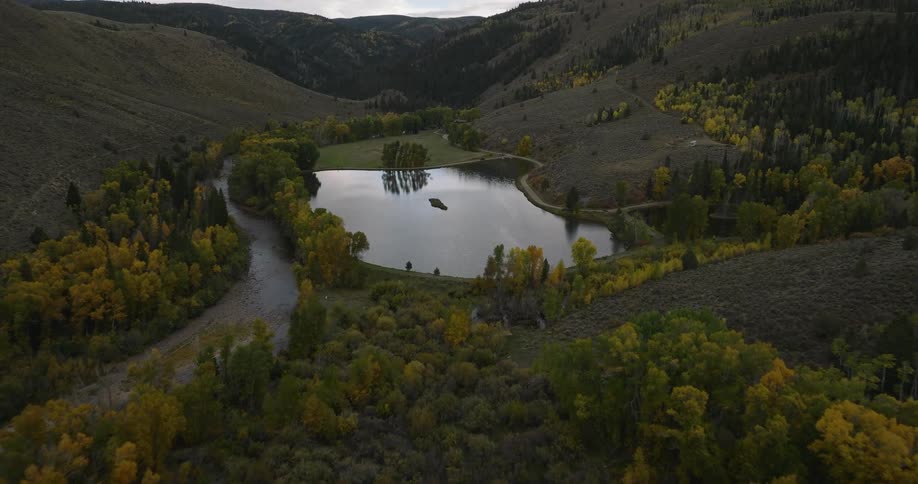 Aerial view of a small lake surrounded by hills and trees with fall colors