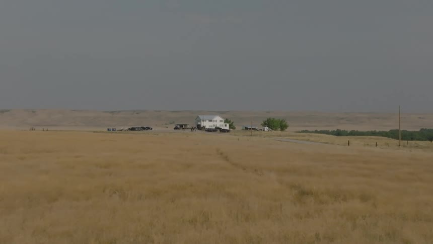 A large rural farmhouse sits at the end of a very large grassy field