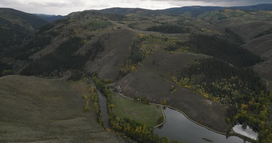 A wide aerial view of rolling hills with patches of trees and a small reflective lake