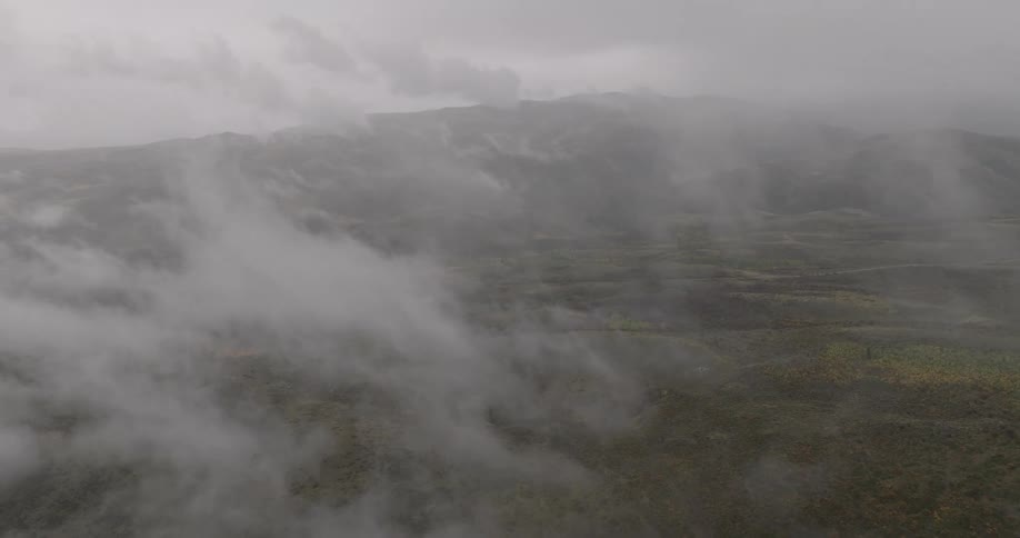 A vast mountainous landscape is enveloped in dense clouds and fog creating an ethereal and moody atmosphere