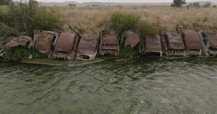Row of abandoned rusted cars on the edge of a river bed in the country