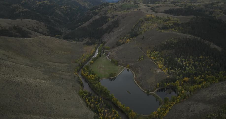 Aerial view of a river winding through a mountainous valley with scattered autumn trees
