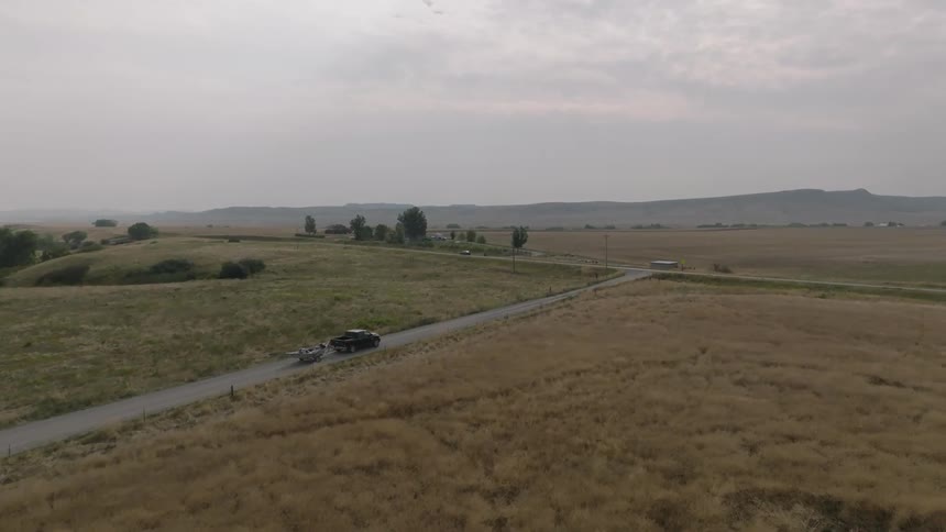 Aerial of a truck towing a boat on a road in the middle of a rural area during daytime