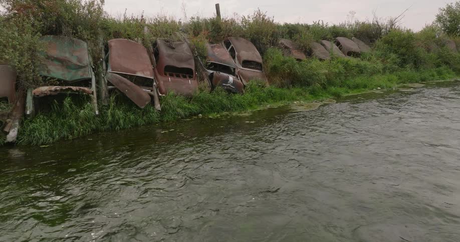 Row of abandoned rusted cars on the edge of a river bed in the country
