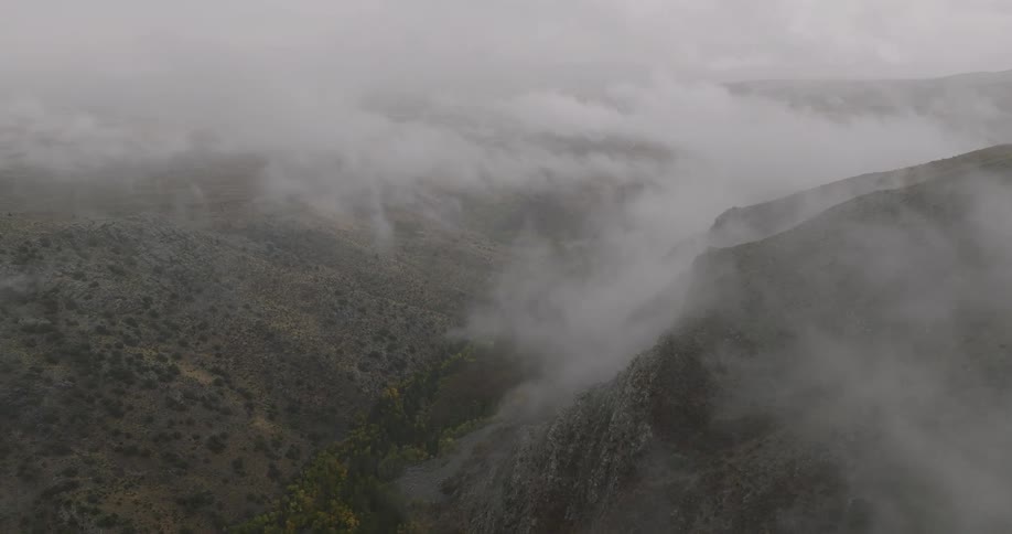 Fog drifts through a rugged canyon landscape with steep cliffs and sparse vegetation