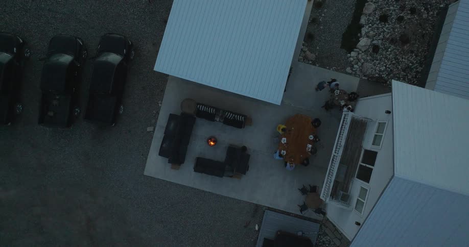 Aerial view of a patio with a fire pit surrounded by chairs a group of people gathered at a nearby table and a building along one edge