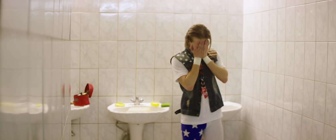 A man walks into a bathroom and wipes his face