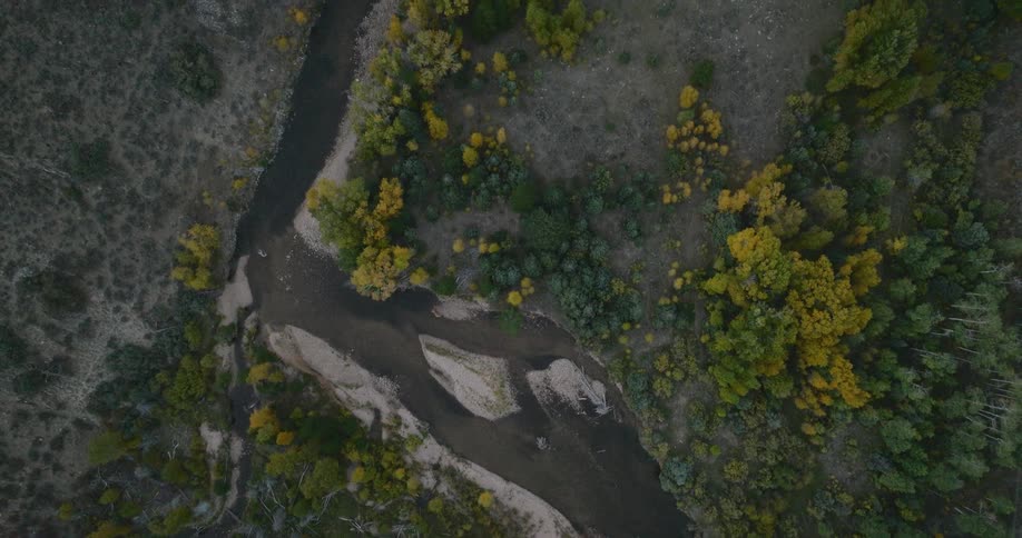 Aerial view of a winding river cutting through a forest with trees in fall colors