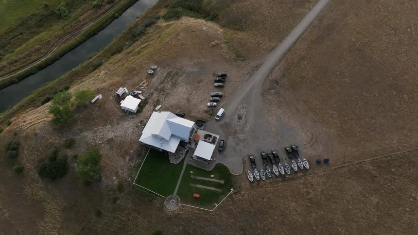 Aerial view of a rural property with buildings parked vehicles and nearby canal