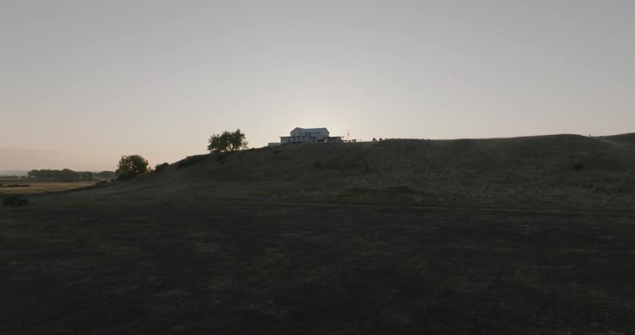 Sun cresting a hilltop shines past a rural home