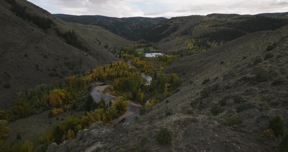 A river winds through a valley surrounded by forested hills and autumn trees