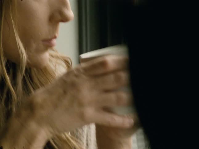 A woman takes a sip of a drink in a mug and smiles up at someone