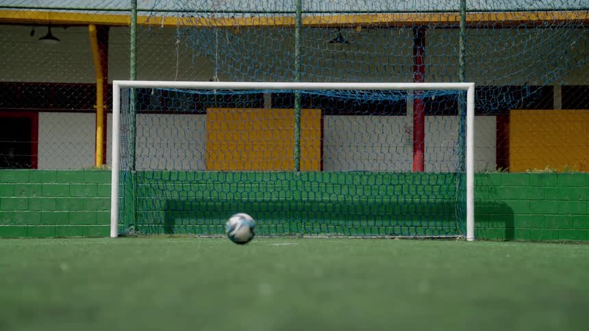 A soccer ball rests in the center of a goalpost on an empty field