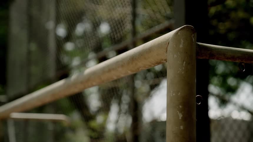 Water droplets cling to a weathered metal railing in front of a chainlink fence and outoffocus foliage