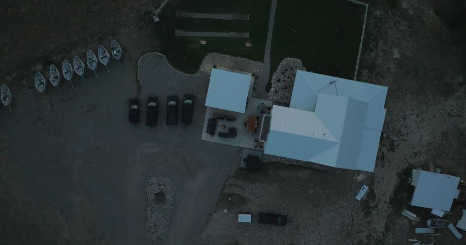 Top down aerial view of buildings cars and boats near a gravel lot at dusk