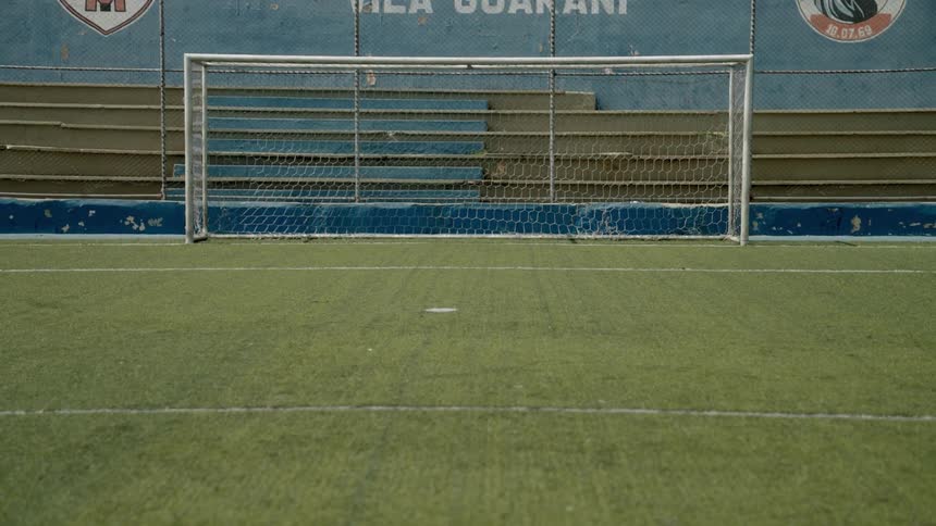 An empty indoor soccer goal on a green turf field with bleachers behind