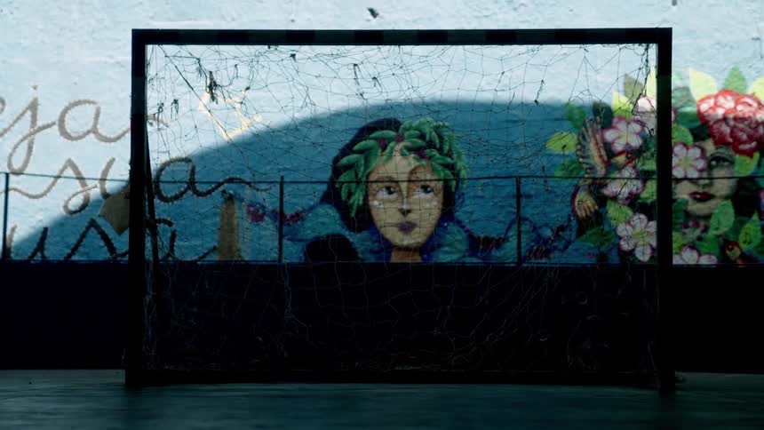 A dark worn soccer goal stands in front of a colorful mural featuring faces and flowers