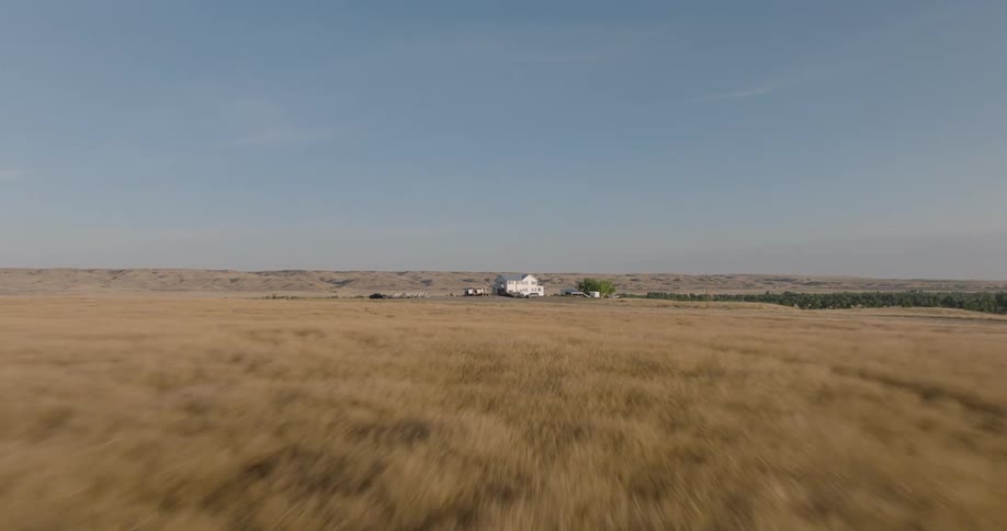 A white house sits alone at the end of a large rural grasscovered field