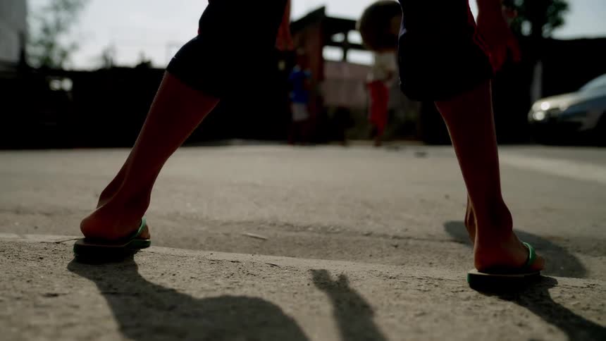 Close up of a boys legs as he positions to catch a shot played at him by his friends on a street during daytime