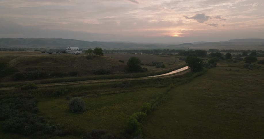 A large white house stands alone atop a hill near a river at sunset