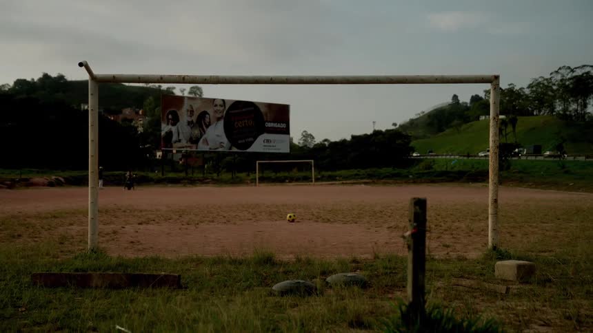A soccer goalpost stands on a dirt field with a ball in front