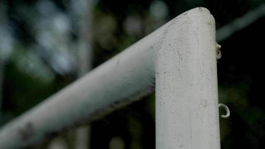 A closeup shot focuses on the weathered whitepainted corner of a soccer goal post with a blurry outdoor background