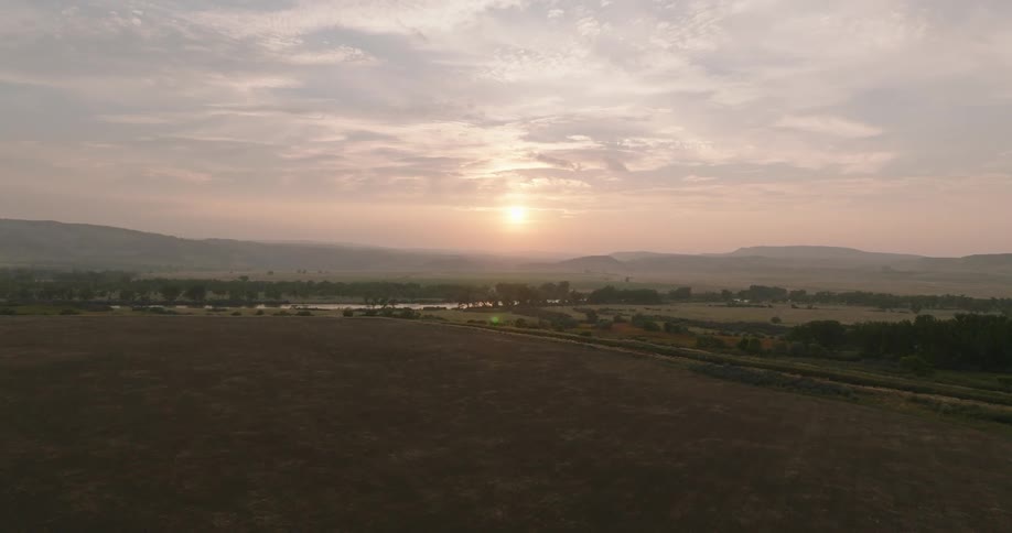 A scenic rural landscape is captured at sunrise with soft clouds and distant hills