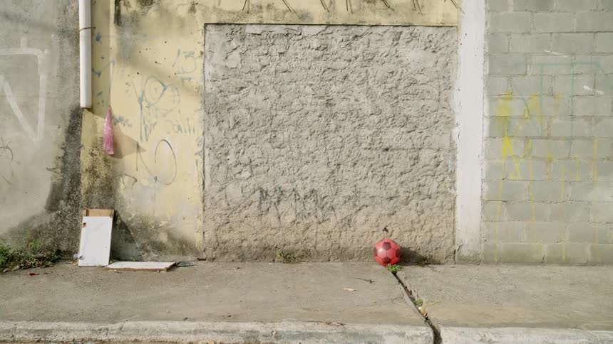A red soccer ball rests against a rough slightly graffitied wall