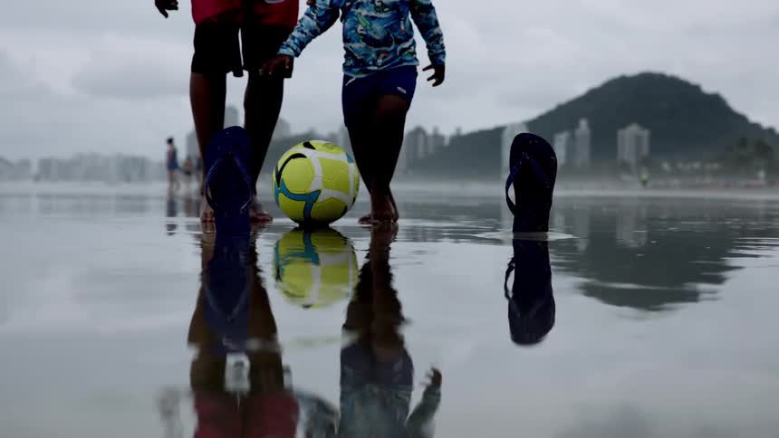A person and child play with a soccer ball on the beach