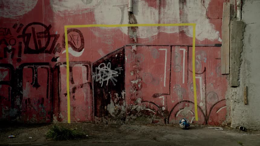 A soccer ball lies in front of a graffiti covered wall with a yellow goal outline painted on it