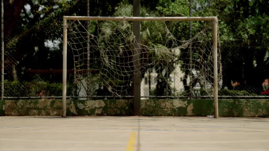 A weathered soccer goal with a torn and sagging net on an empty outdoor concrete court