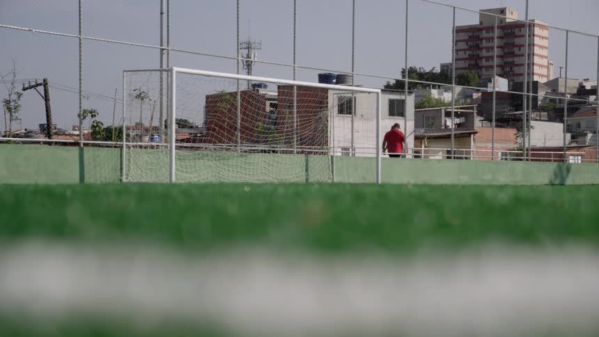 A soccer goalpost on a turf field with urban buildings and fencing in the background