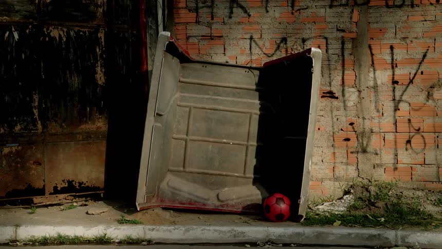 A red soccer ball rests inside an overturned metal container against a graffiti covered brick wall