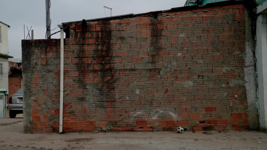 Soccer balls sit in front of a stained brick wall in a bare alleyway