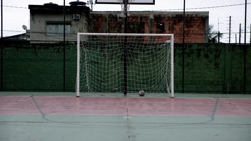 A ball in a netted goalpost in an outdoor soccer play area during daytime