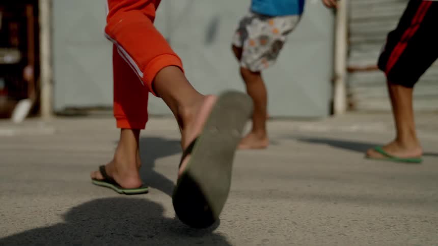 Close of male childrens legs as they play soccer outdoors on a street during daytime