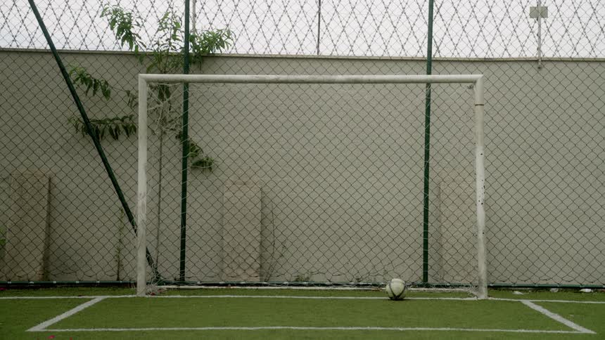 A soccer goalpost with a ball resting near the line on an empty turf field