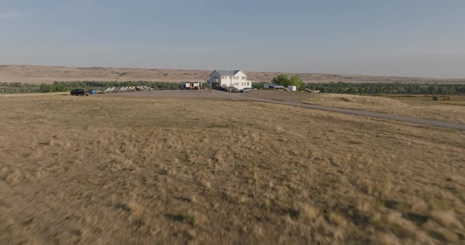 Aerial view of a large open field with a house and several parked cars at one end