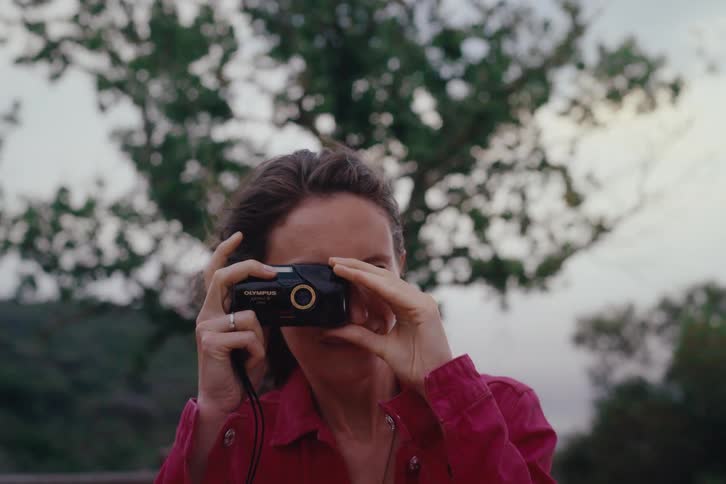 A person in a red shirt is outdoors holding a camera up to take a picture